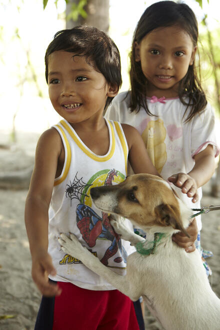 Boy and girl standing with dog reaching up, Philippines. GARC