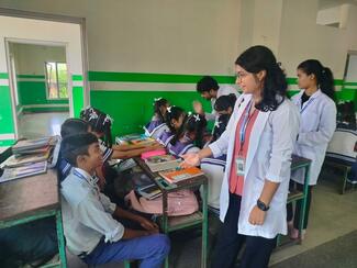 Vet student volunteer wearing a white coat talking to school children.
