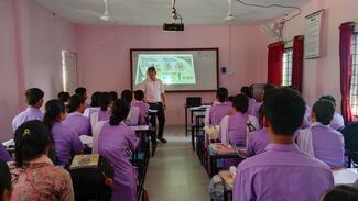 "Image showing a group of PCL 1st-year nursing students attentively listening to a presentation on rabies and its prevention. The presenter,Mr Anup Muni Bajracharya, Microbiologists, explains the transmission, symptoms, and preventive measures of rabies, including vaccination and proper wound care. Educational posters or slides about rabies displayed in the background."
